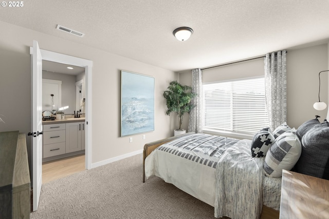 bedroom with visible vents, light carpet, a sink, a textured ceiling, and baseboards