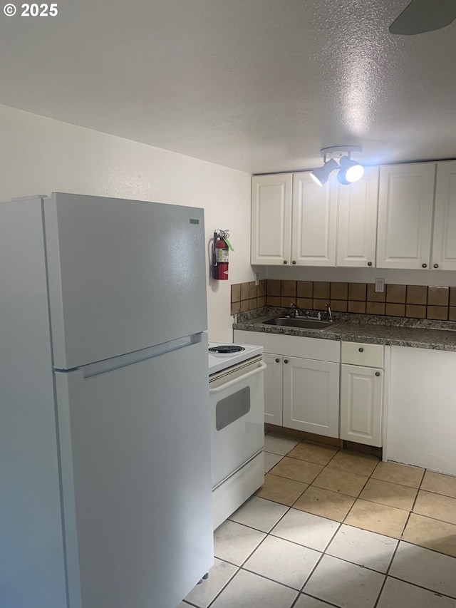 kitchen featuring dark countertops, white appliances, white cabinetry, and a sink