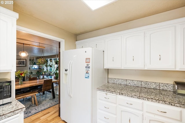 5770 SW Cranberry Ct, Beaverton, OR 97007 - kitchen with white refrigerator with ice dispenser, tile countertops, stainless steel microwave, light wood-style floors, and white cabinets