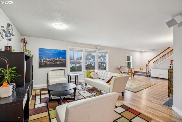 living area featuring light wood-style flooring, baseboards, stairway, and a textured ceiling