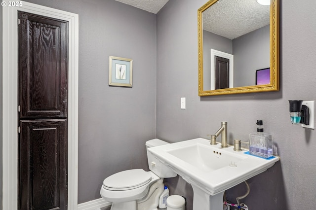 bathroom featuring a textured ceiling, a sink, toilet, and baseboards