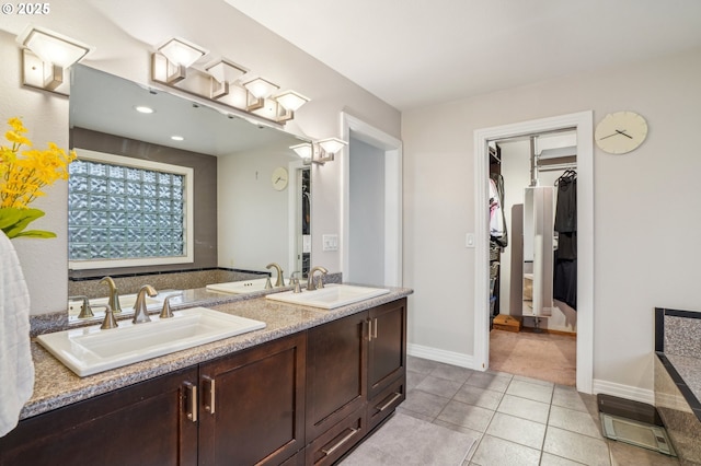 bathroom featuring double vanity, a walk in closet, a sink, and tile patterned floors