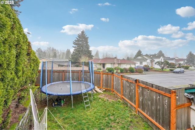 view of yard featuring a trampoline, a fenced backyard, and a residential view