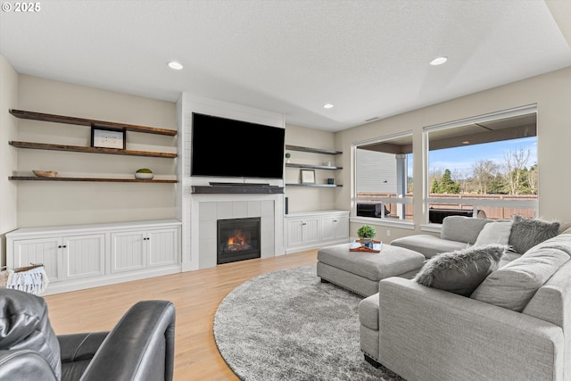 living room with a textured ceiling, light wood finished floors, a tile fireplace, and recessed lighting