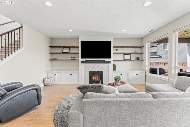 living room with visible vents, a tile fireplace, stairway, light wood-type flooring, and recessed lighting