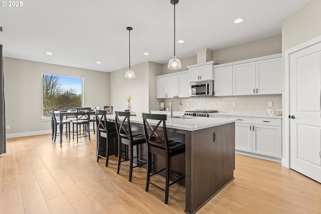 kitchen with white cabinets, stainless steel microwave, a sink, a kitchen bar, and backsplash