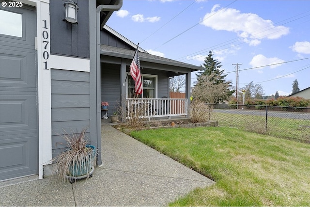 doorway to property featuring covered porch, a yard, and fence