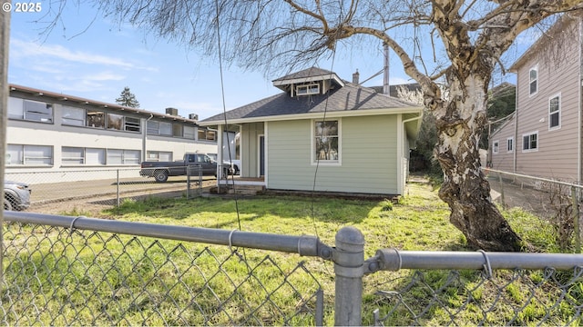 rear view of house with roof with shingles, a lawn, and fence