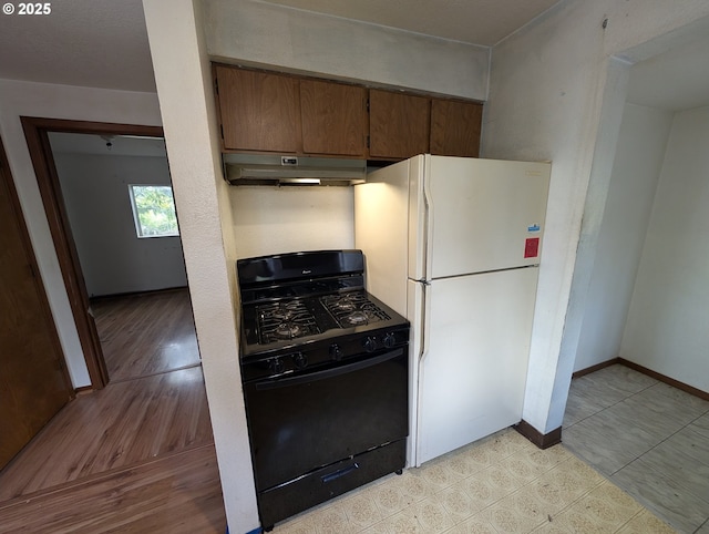 10539 NW 3rd St, Portland, OR 97231 - kitchen with black range with gas cooktop, freestanding refrigerator, under cabinet range hood, baseboards, and brown cabinetry