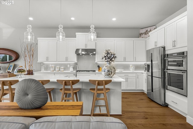 kitchen featuring light countertops, white cabinets, dark wood-type flooring, under cabinet range hood, and appliances with stainless steel finishes