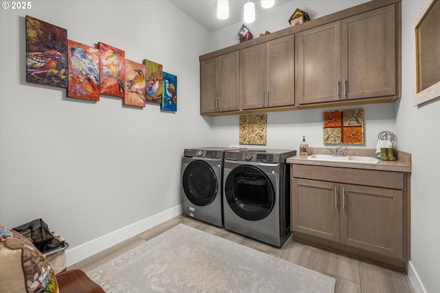 washroom featuring a sink, cabinet space, light wood-style floors, and washing machine and dryer