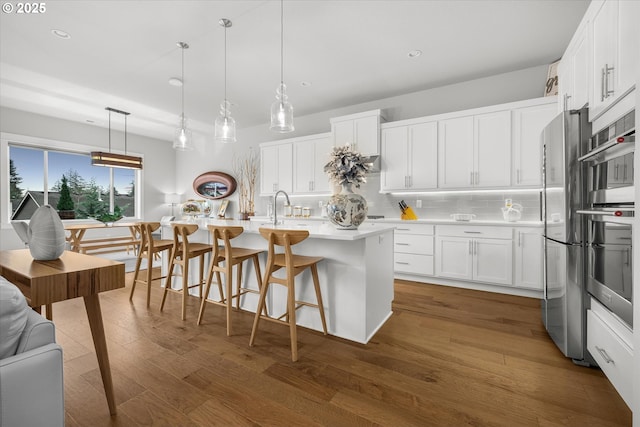 kitchen with backsplash, dark wood finished floors, a breakfast bar area, light countertops, and white cabinets