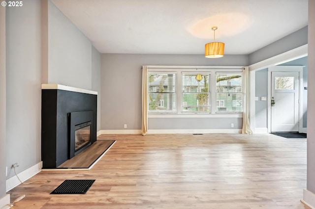 living area with visible vents, baseboards, a glass covered fireplace, and wood finished floors