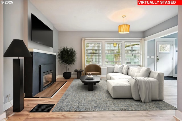 living area featuring a glass covered fireplace, visible vents, baseboards, and wood finished floors