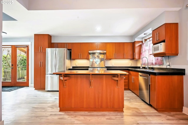 kitchen with a center island, under cabinet range hood, brown cabinetry, stainless steel appliances, and a sink