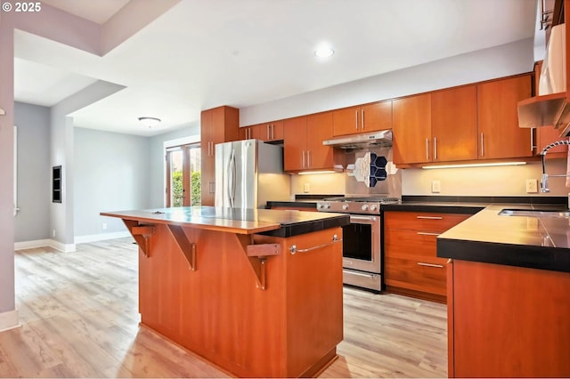 kitchen with under cabinet range hood, brown cabinets, appliances with stainless steel finishes, light wood-style floors, and a sink