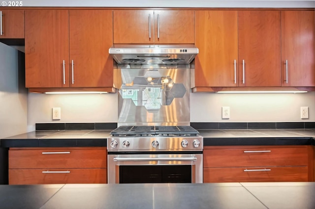 kitchen with under cabinet range hood, brown cabinetry, and stainless steel gas range