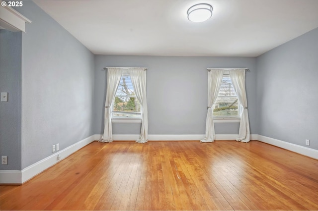 empty room featuring a healthy amount of sunlight, baseboards, and wood-type flooring