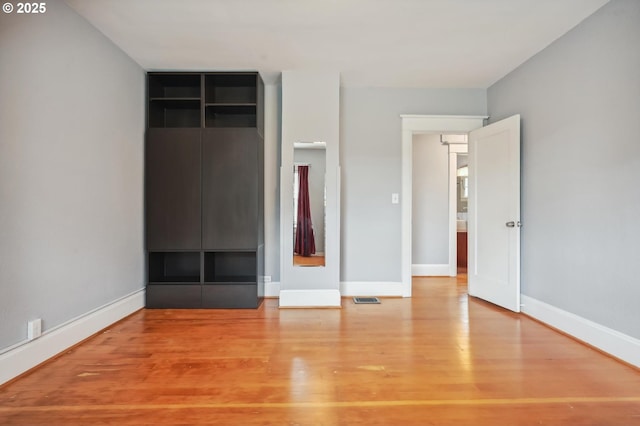 unfurnished bedroom featuring visible vents, baseboards, a closet, and wood finished floors