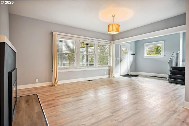 unfurnished living room featuring visible vents, stairway, light wood-style floors, and baseboards