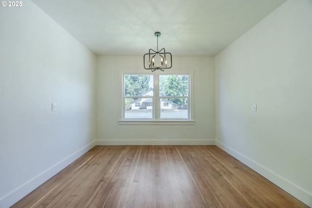 unfurnished dining area with a chandelier, baseboards, and hardwood / wood-style flooring
