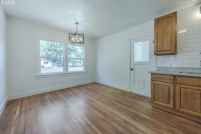 unfurnished dining area featuring a chandelier, light wood finished floors, baseboards, and a sink