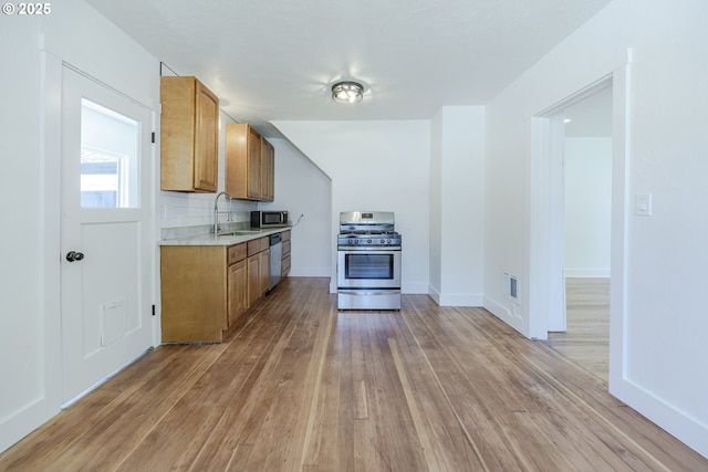 kitchen with appliances with stainless steel finishes, a sink, light countertops, light wood-style flooring, and brown cabinetry