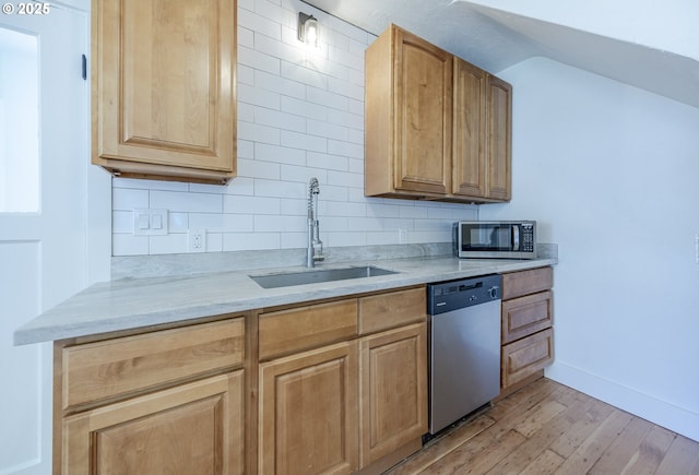 kitchen with stainless steel appliances, a sink, light wood finished floors, backsplash, and baseboards