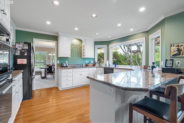 kitchen with ornamental molding, black appliances, a sink, a peninsula, and light wood-style flooring
