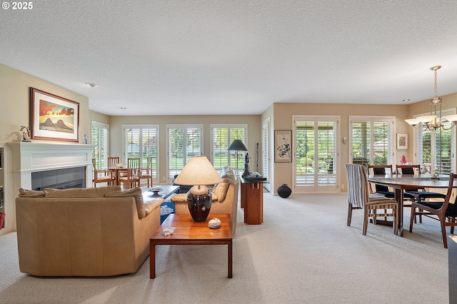 living room with a textured ceiling, a chandelier, a tile fireplace, plenty of natural light, and light carpet