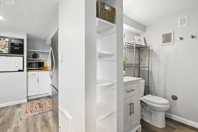 bathroom with wood finished floors, toilet, baseboards, and vanity