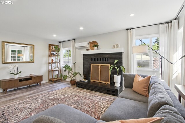 living area featuring a wall mounted AC, a fireplace with raised hearth, wood finished floors, and recessed lighting