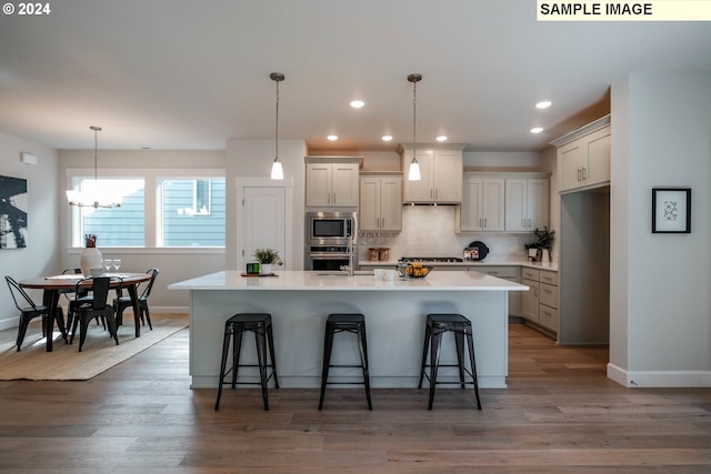 kitchen with appliances with stainless steel finishes, backsplash, hardwood / wood-style floors, a kitchen breakfast bar, and an island with sink