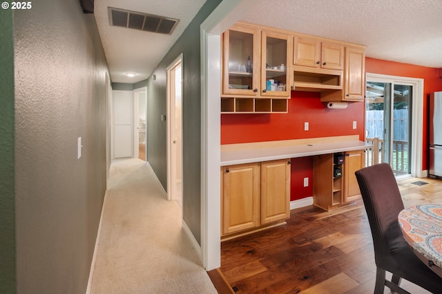 1378 SW Taylors Ferry Ct, Portland, OR 97219 - kitchen with freestanding refrigerator, a textured ceiling, glass insert cabinets, light brown cabinetry, and wood finished floors