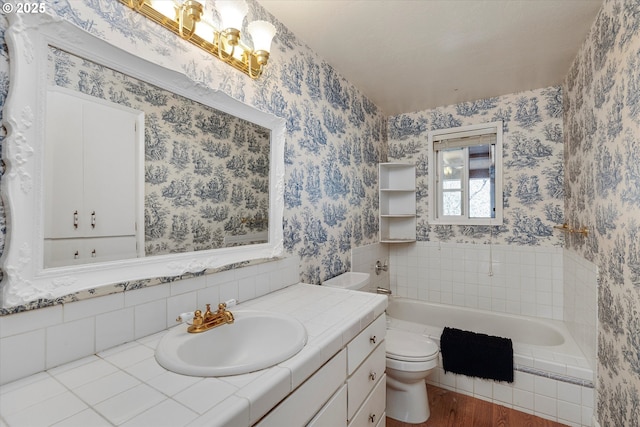 full bathroom with a relaxing tiled tub, vanity, toilet, and wallpapered walls