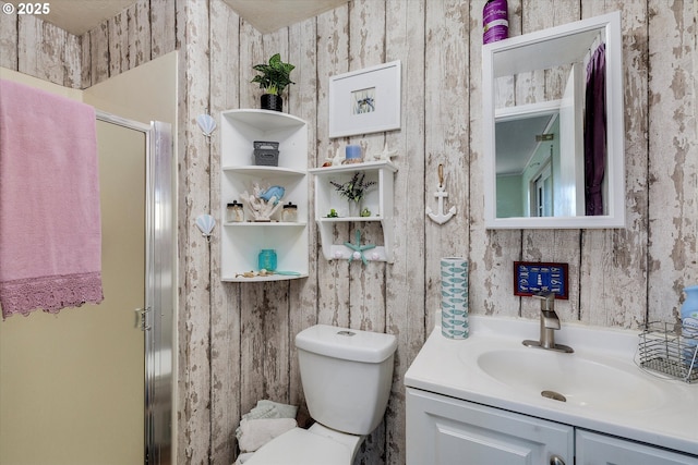 bathroom with toilet, wallpapered walls, vanity, and a stall shower