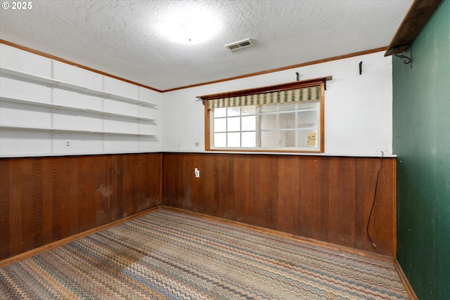 carpeted spare room with ornamental molding, visible vents, wooden walls, and a textured ceiling