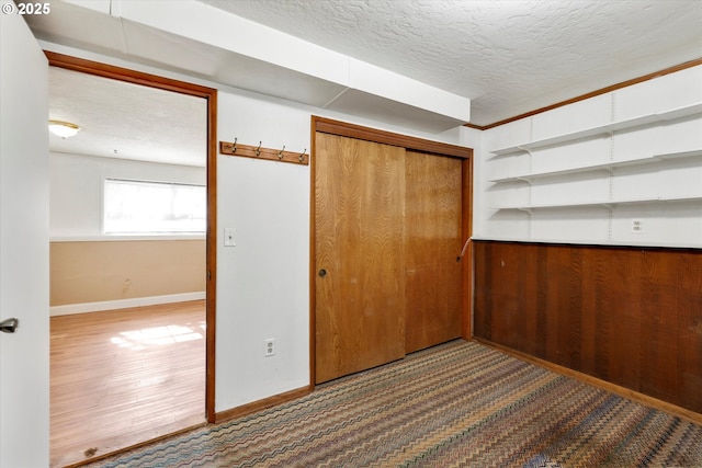 unfurnished bedroom featuring a closet, baseboards, a textured ceiling, and wood finished floors