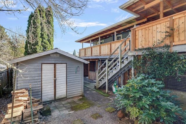 rear view of property with stairs, an outdoor structure, fence, and a storage unit