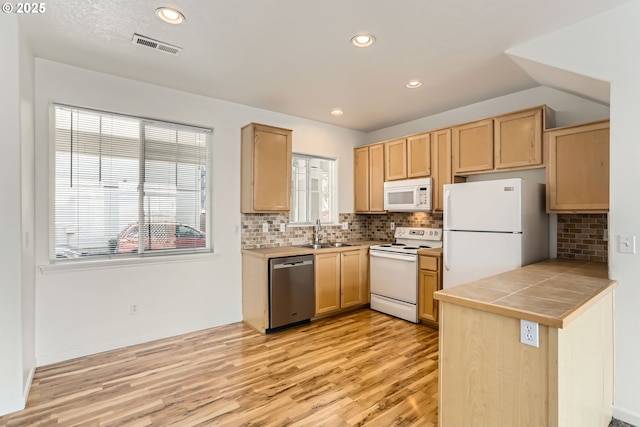kitchen featuring light brown cabinetry, a sink, tile counters, white appliances, and light wood-style flooring