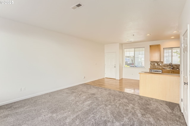 unfurnished living room with light colored carpet, a sink, recessed lighting, baseboards, and visible vents