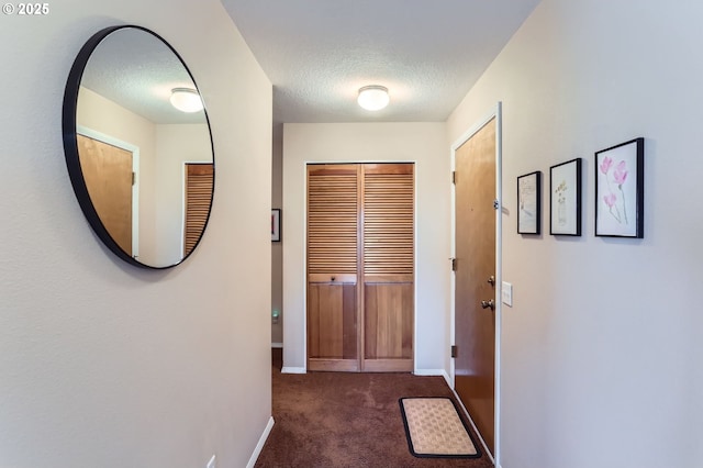 entryway featuring dark colored carpet, a textured ceiling, and baseboards