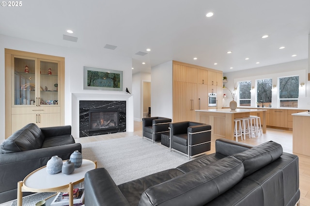 living room featuring recessed lighting, visible vents, light wood-style flooring, and a high end fireplace