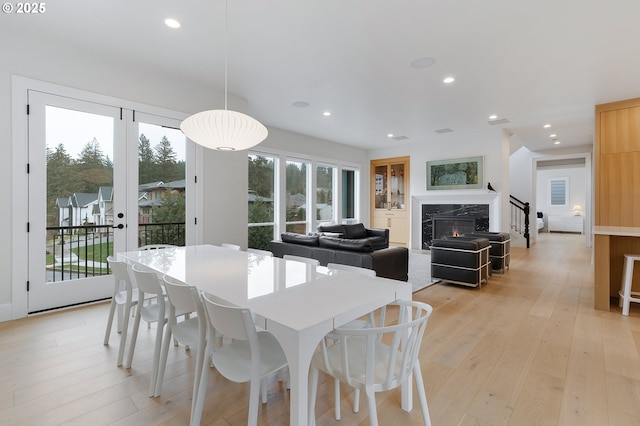 dining space featuring light wood-style flooring, recessed lighting, french doors, and a premium fireplace