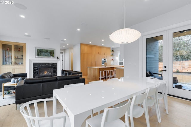 dining room featuring light wood-style flooring, french doors, recessed lighting, and a high end fireplace