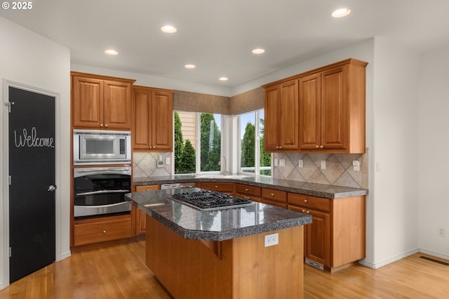 kitchen featuring light wood-type flooring, tasteful backsplash, a center island, and stainless steel appliances