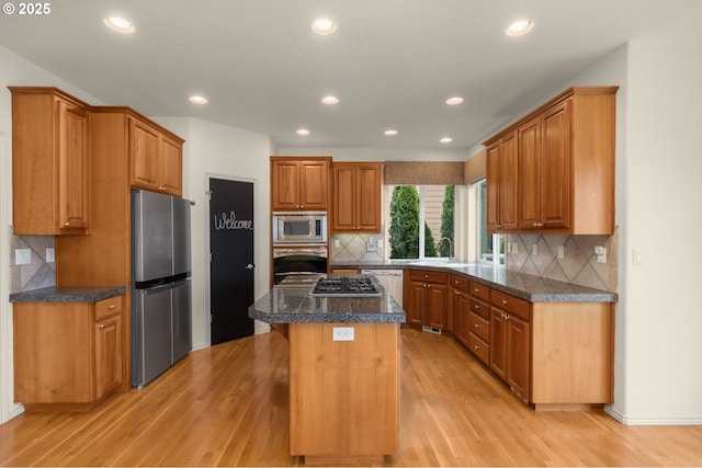 kitchen featuring brown cabinets, appliances with stainless steel finishes, light wood finished floors, decorative backsplash, and a kitchen island