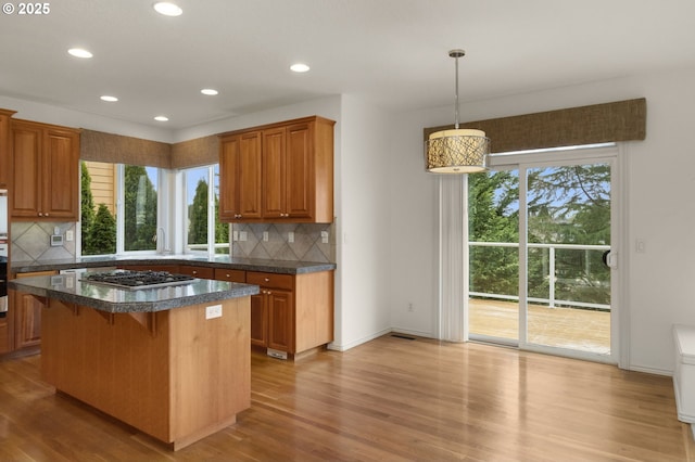kitchen featuring decorative backsplash, brown cabinetry, dark countertops, stainless steel gas cooktop, and light wood-style flooring