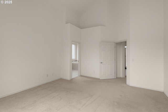 unfurnished room featuring a high ceiling, light colored carpet, and baseboards