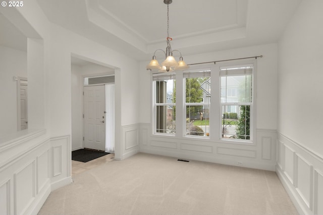 unfurnished dining area featuring light colored carpet, visible vents, a raised ceiling, and a decorative wall